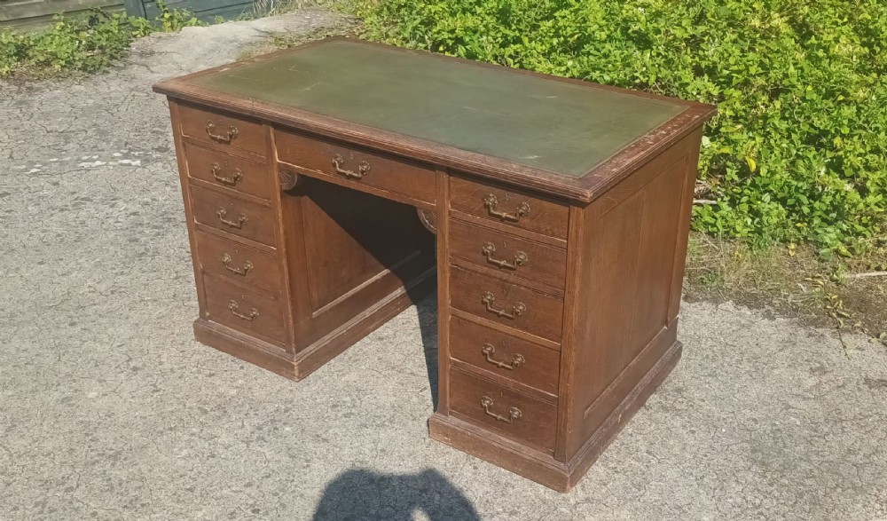 A late Victorian oak kneehole pedestal writing desk featuring nine drawers with brass handles and a green leather insert on the top surface. View VIII
