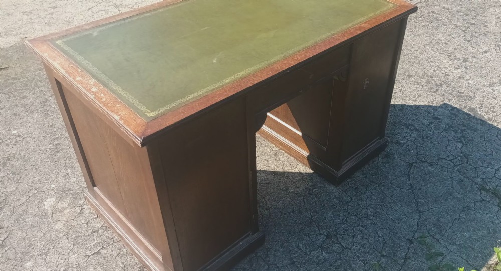 A late Victorian oak kneehole pedestal writing desk featuring nine drawers with brass handles and a green leather insert on the top surface. View IX
