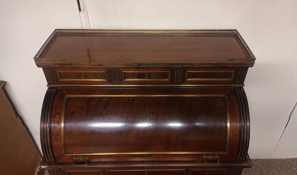 An antique French mahogany cylinder bureau featuring brass mouldings, a top pierced brass gallery, frieze drawers, and fluted legs. View II