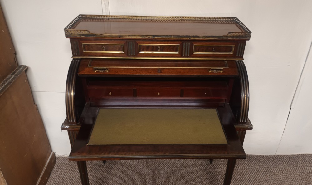 An antique French mahogany cylinder bureau featuring brass mouldings, a top pierced brass gallery, frieze drawers, and fluted legs. View III