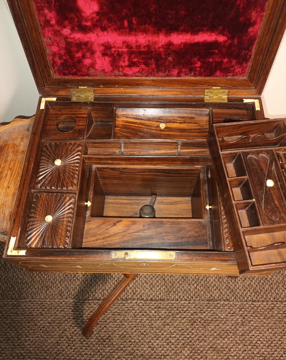 An Anglo-Indian rosewood work table featuring a hinged lid with velvet lining, fitted internal compartments, bone inlay, drop-leaf flaps, a spindle gallery, and a tripod pedestal base. View II