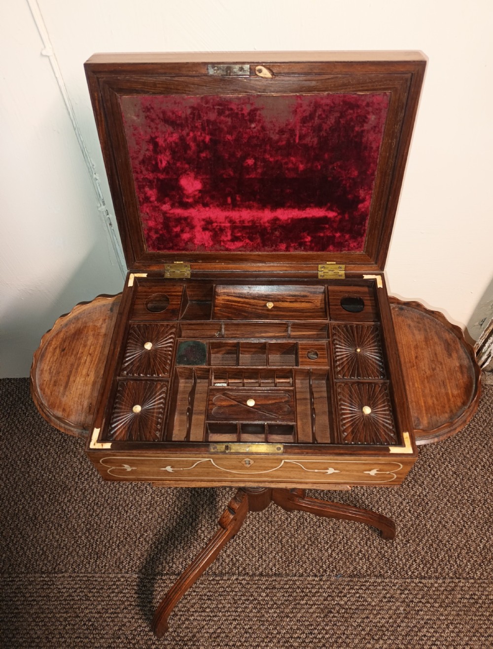 An Anglo-Indian rosewood work table featuring a hinged lid with velvet lining, fitted internal compartments, bone inlay, drop-leaf flaps, a spindle gallery, and a tripod pedestal base. View III