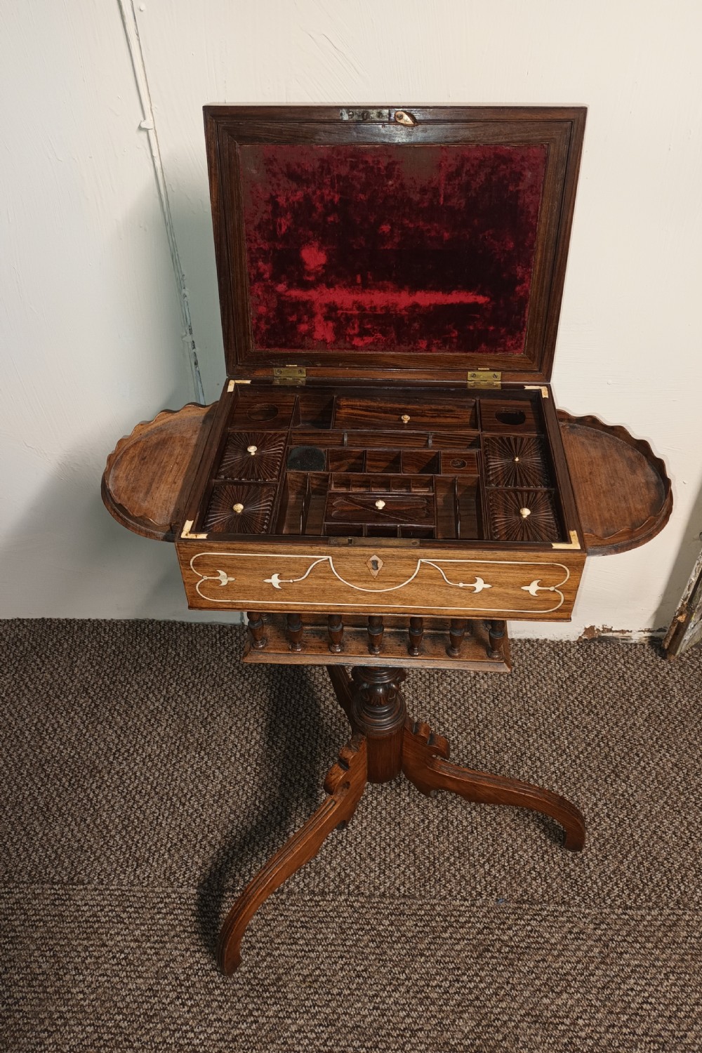 An Anglo-Indian rosewood work table featuring a hinged lid with velvet lining, fitted internal compartments, bone inlay, drop-leaf flaps, a spindle gallery, and a tripod pedestal base. View IV