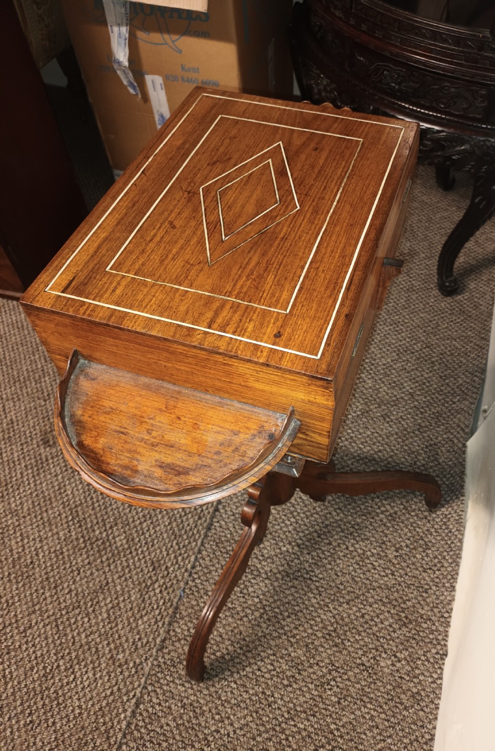 An Anglo-Indian rosewood work table featuring a hinged lid with velvet lining, fitted internal compartments, bone inlay, drop-leaf flaps, a spindle gallery, and a tripod pedestal base. View X