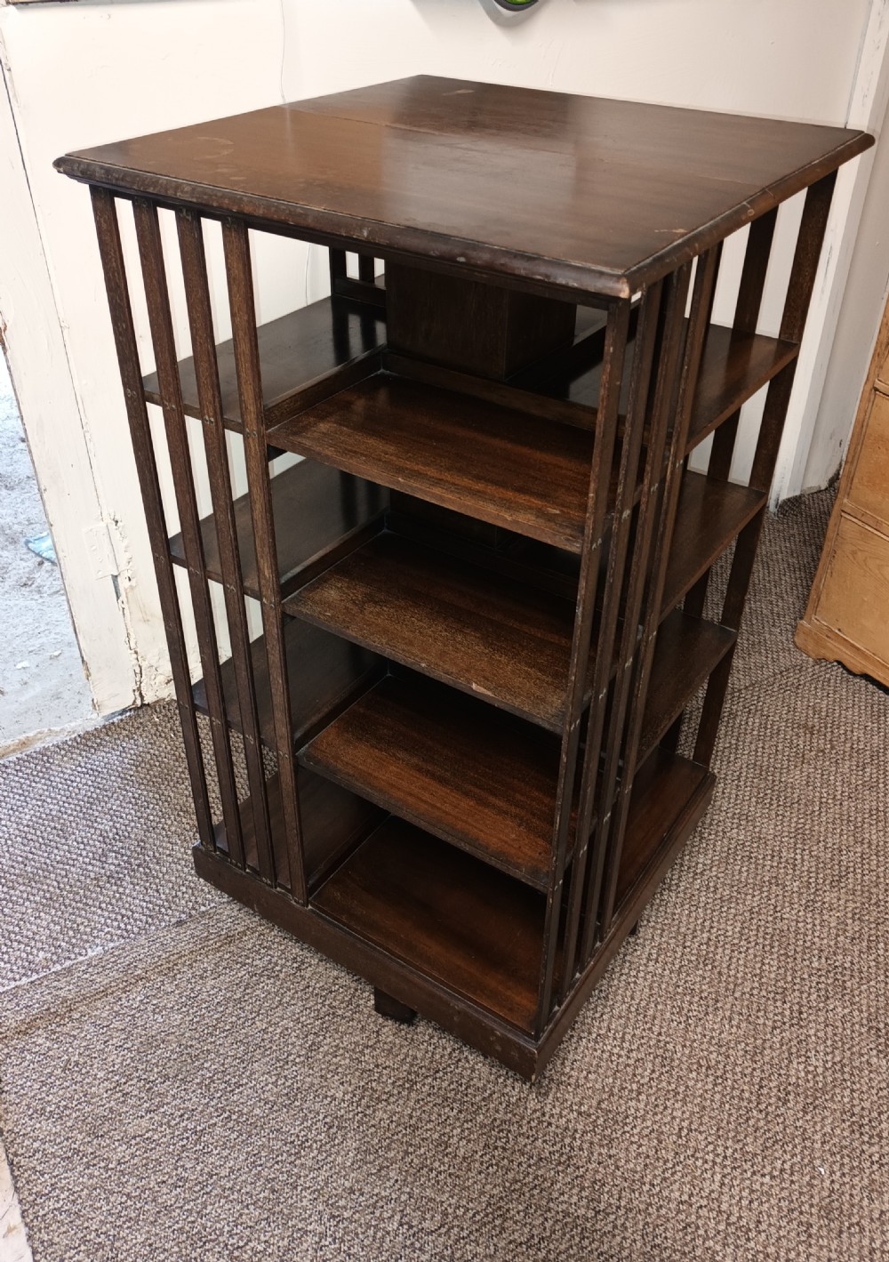 A square dark mahogany revolving bookcase featuring multi-tiered shelves and vertical side slats. View VI
