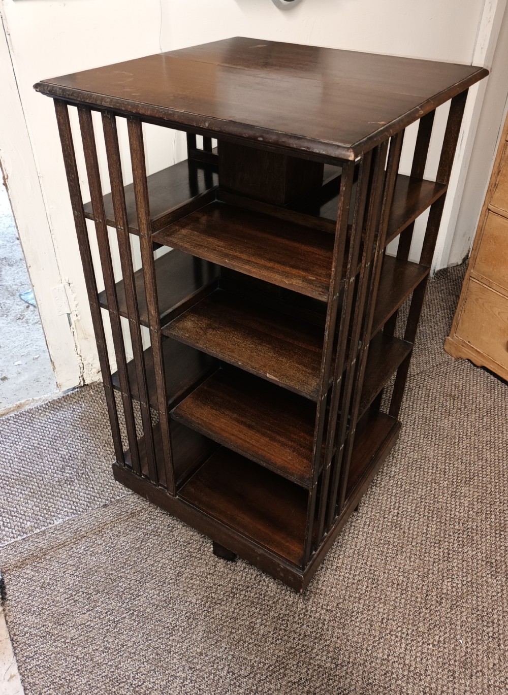 A square dark mahogany revolving bookcase featuring multi-tiered shelves and vertical side slats. View VII