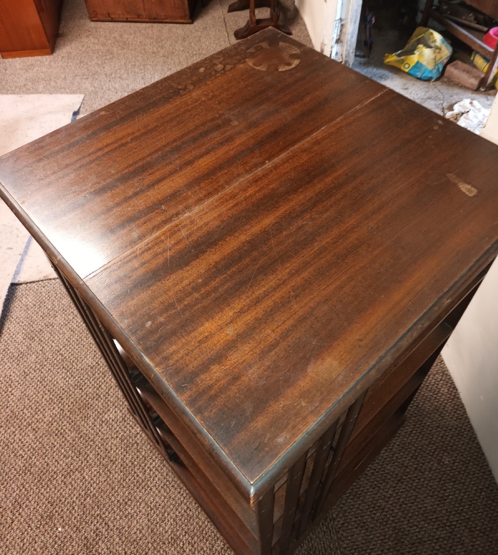 A square dark mahogany revolving bookcase featuring multi-tiered shelves and vertical side slats. View X
