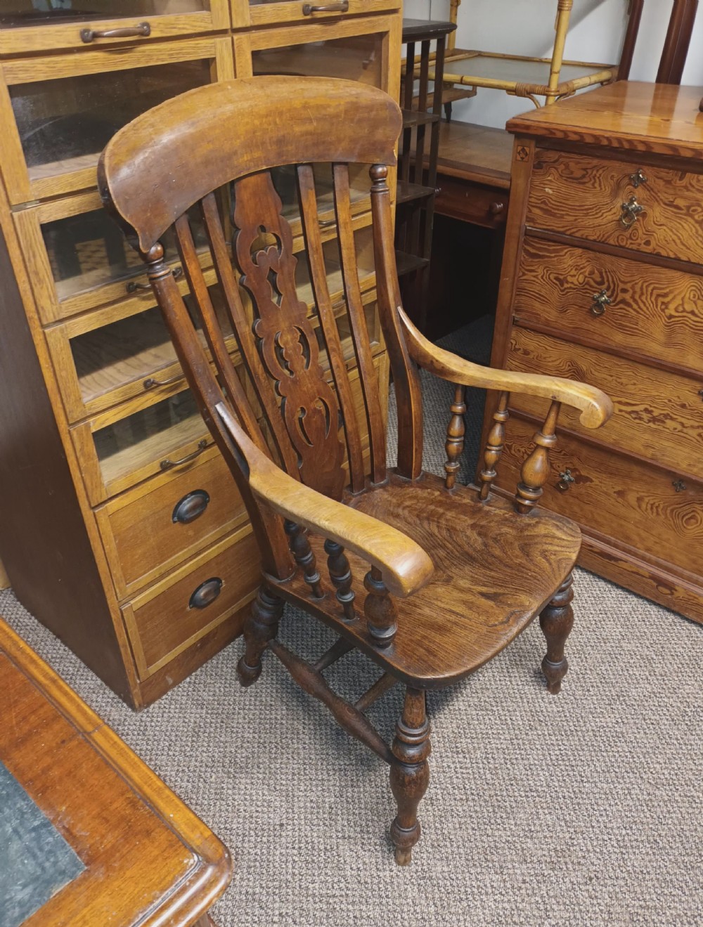 A dark-stained Victorian Windsor armchair with a spindled high back, carved central splat, shaped armrests, solid seat, and turned wooden legs. View III