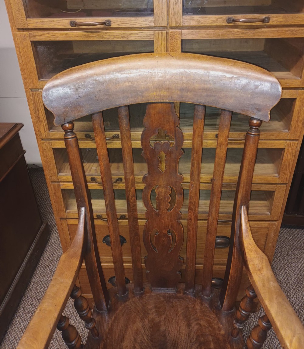 A dark-stained Victorian Windsor armchair with a spindled high back, carved central splat, shaped armrests, solid seat, and turned wooden legs. View IV