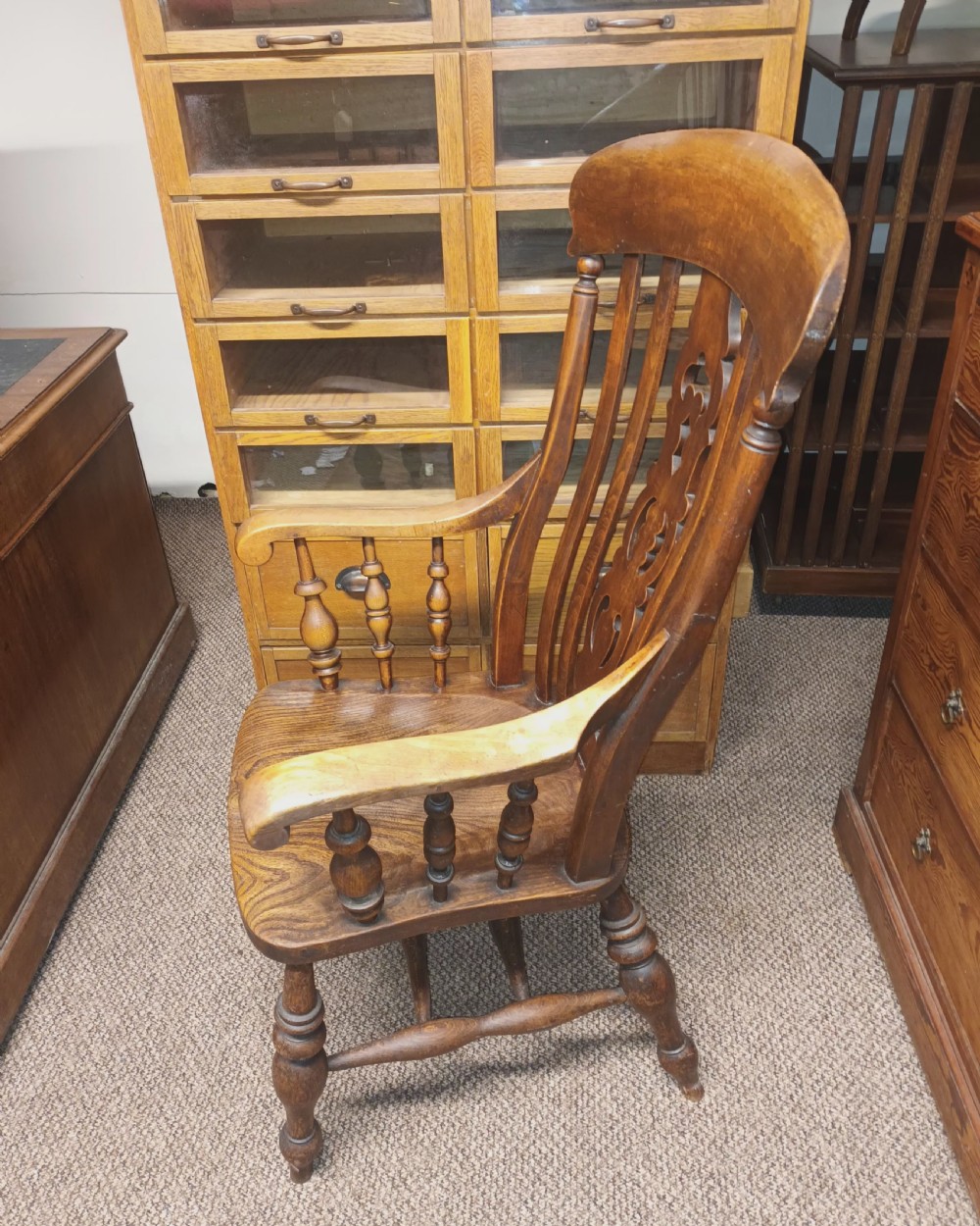 A dark-stained Victorian Windsor armchair with a spindled high back, carved central splat, shaped armrests, solid seat, and turned wooden legs. View VI