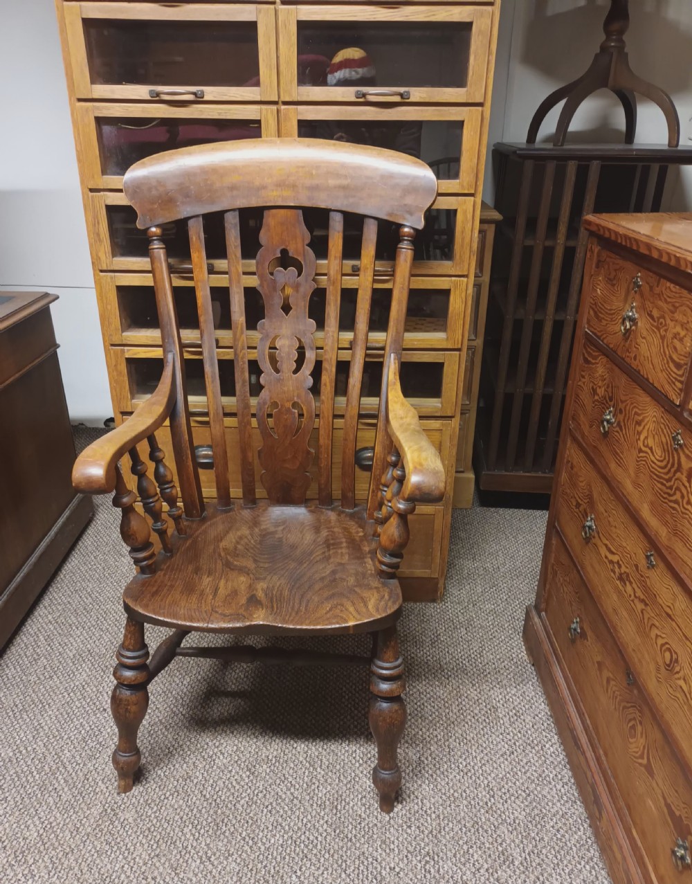 A dark-stained Victorian Windsor armchair with a spindled high back, carved central splat, shaped armrests, solid seat, and turned wooden legs. View VII