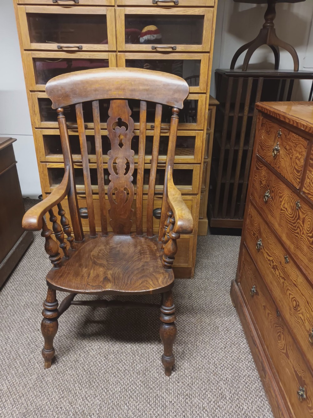 A dark-stained Victorian Windsor armchair with a spindled high back, carved central splat, shaped armrests, solid seat, and turned wooden legs. View VIII