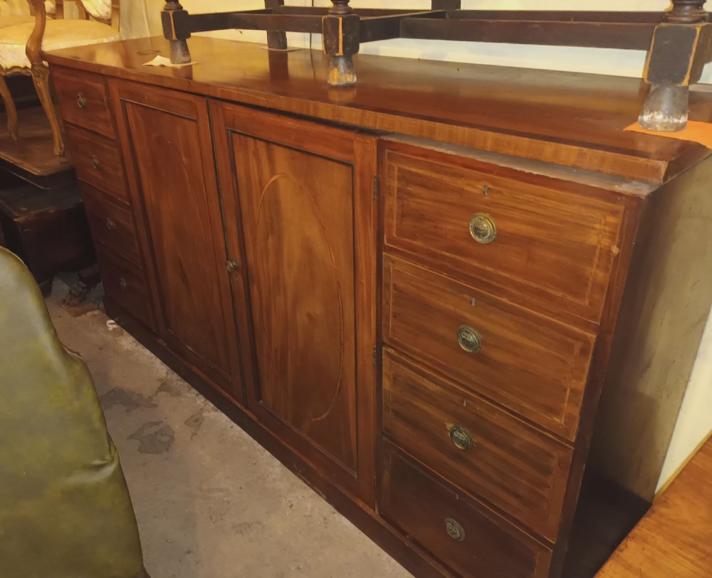 An antique warm brown mahogany dwarf linen press with central inlaid double doors flanked by two stacks of drawers and brass pull handles. View XVIII