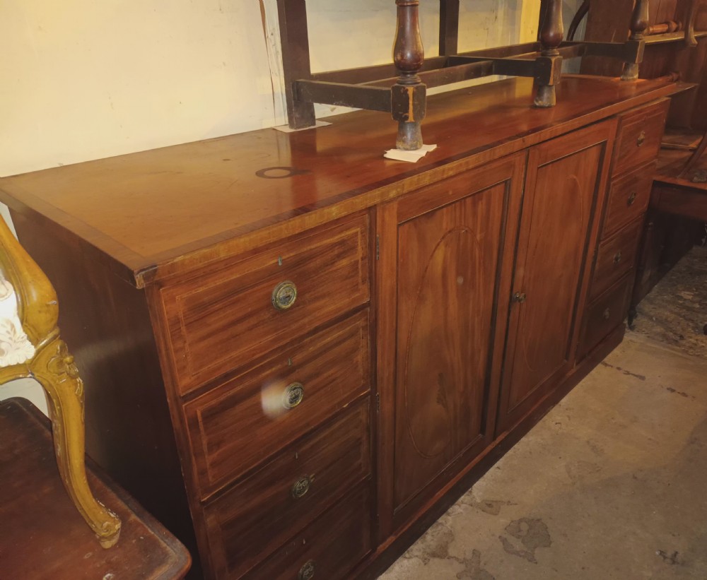 An antique warm brown mahogany dwarf linen press with central inlaid double doors flanked by two stacks of drawers and brass pull handles. View XX