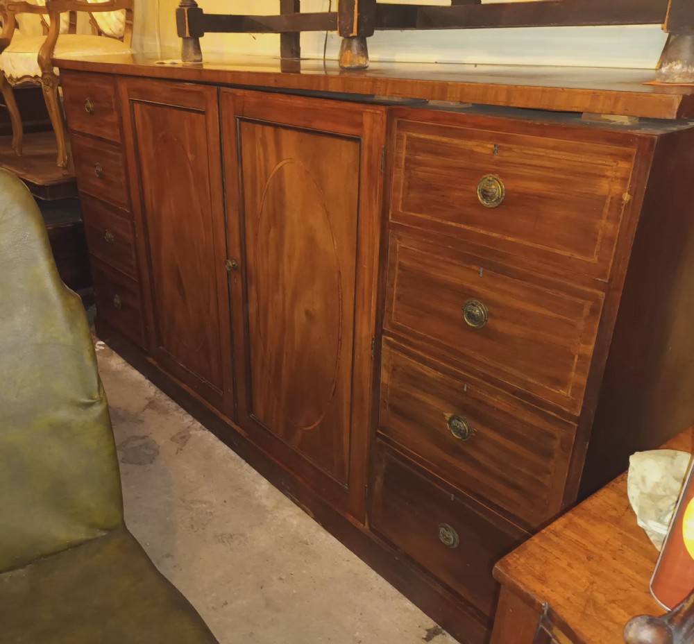 An antique warm brown mahogany dwarf linen press with central inlaid double doors flanked by two stacks of drawers and brass pull handles. View XXVI