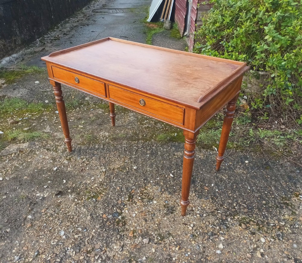 A Victorian mahogany writing table with a raised gallery edge, two front frieze drawers with brass ring handles, and four turned legs. View VI