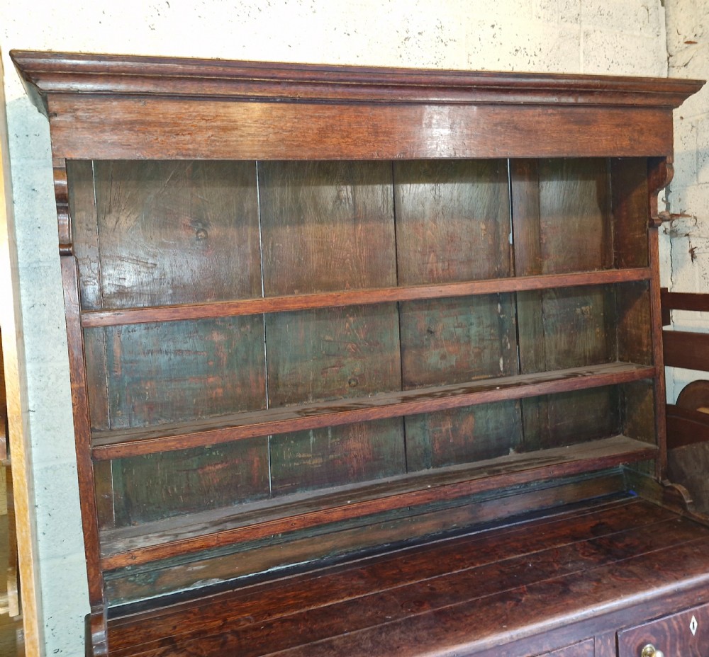 An early 19th-century dark oak Welsh dresser featuring a three-tier open shelving rack above a base with multiple drawers, brass knobs, bone escutcheons, and panelled cupboard doors. View III