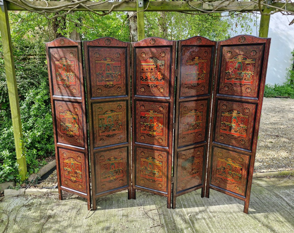 A five-panel Burmese folding screen decorated with red and black lacquered panels depicting detailed architectural scenes.