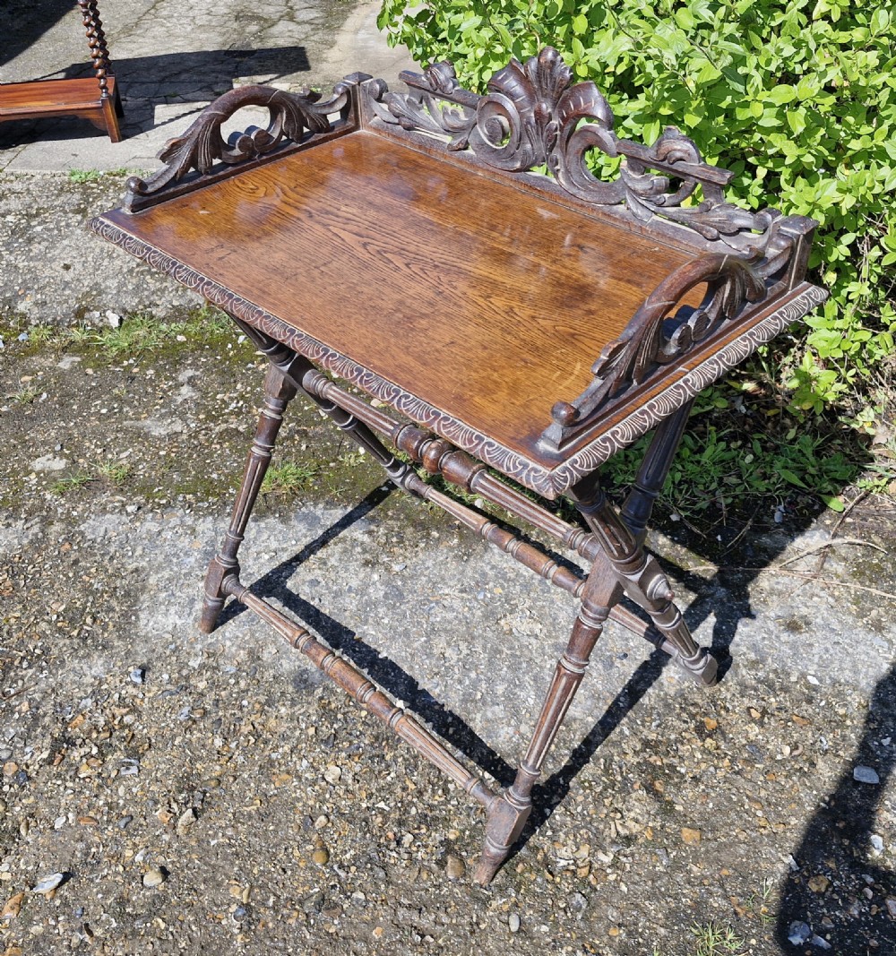 A dark stained Victorian carved oak butlers tray table featuring an intricate carved scrollwork gallery and a folding turned X-frame stand. View II