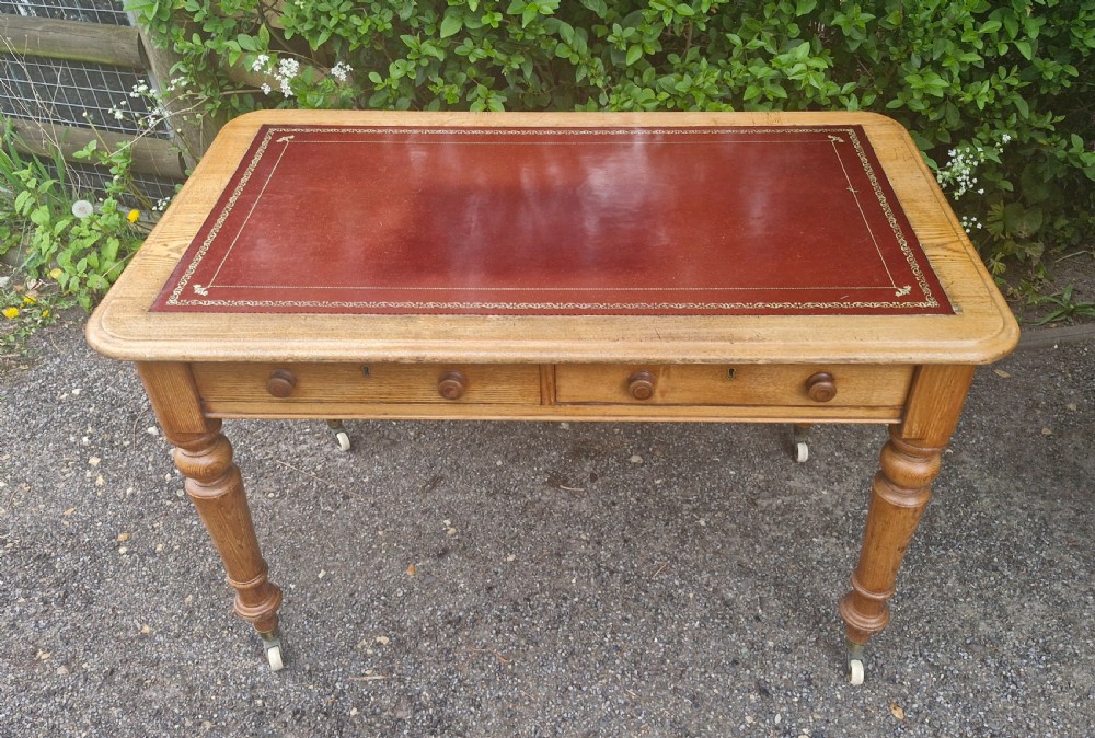A Victorian oak writing table featuring a burgundy leather inset top, two drawers with wooden knobs, turned legs, and brass castors. View III