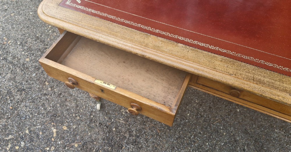 A Victorian oak writing table featuring a burgundy leather inset top, two drawers with wooden knobs, turned legs, and brass castors. View VII