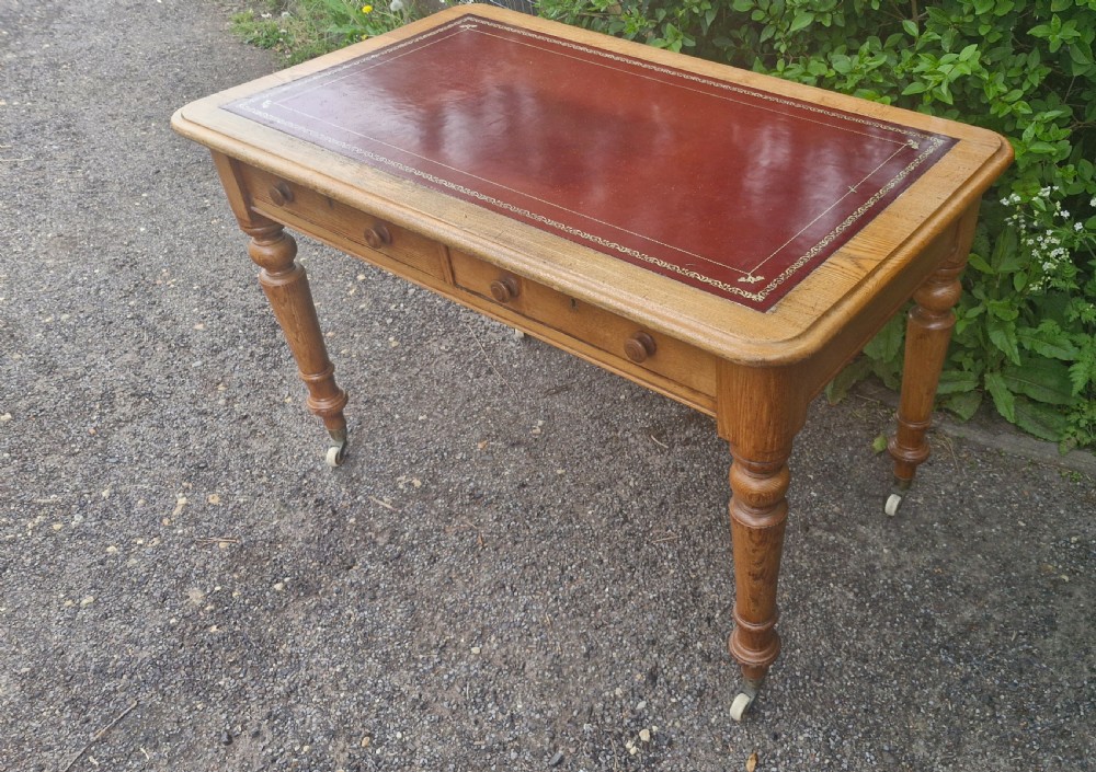 A Victorian oak writing table featuring a burgundy leather inset top, two drawers with wooden knobs, turned legs, and brass castors. View VIII