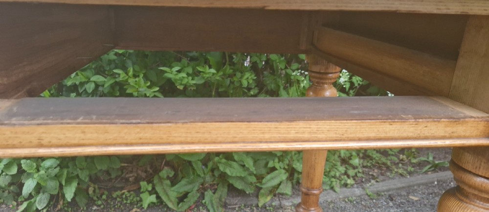 A Victorian oak writing table featuring a burgundy leather inset top, two drawers with wooden knobs, turned legs, and brass castors. View X
