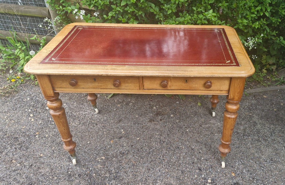 A Victorian oak writing table featuring a burgundy leather inset top, two drawers with wooden knobs, turned legs, and brass castors. View XI