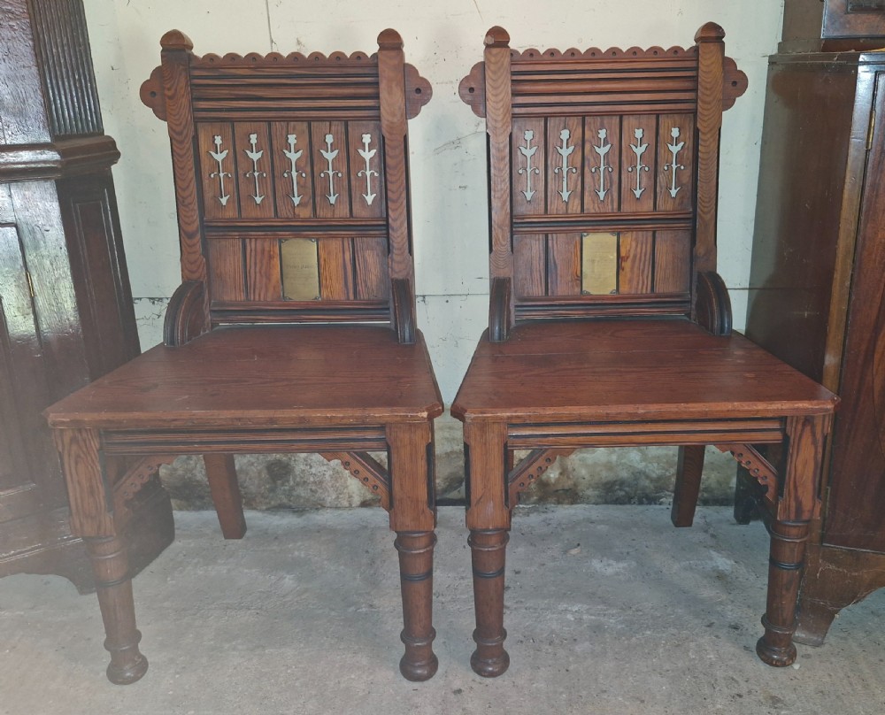 A pair of Victorian pitch pine hall chairs featuring pierced Gothic carved backs, solid wooden seats, and turned front legs. View VI