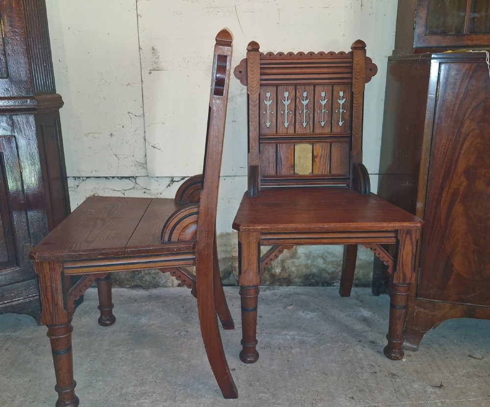 A pair of Victorian pitch pine hall chairs featuring pierced Gothic carved backs, solid wooden seats, and turned front legs. View VII