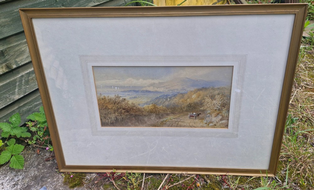 A framed 19th-century watercolour landscape painting showing a horse-drawn cart on a dirt track overlooking hills and the sea, housed within a wide mount and a slim gold frame. View V