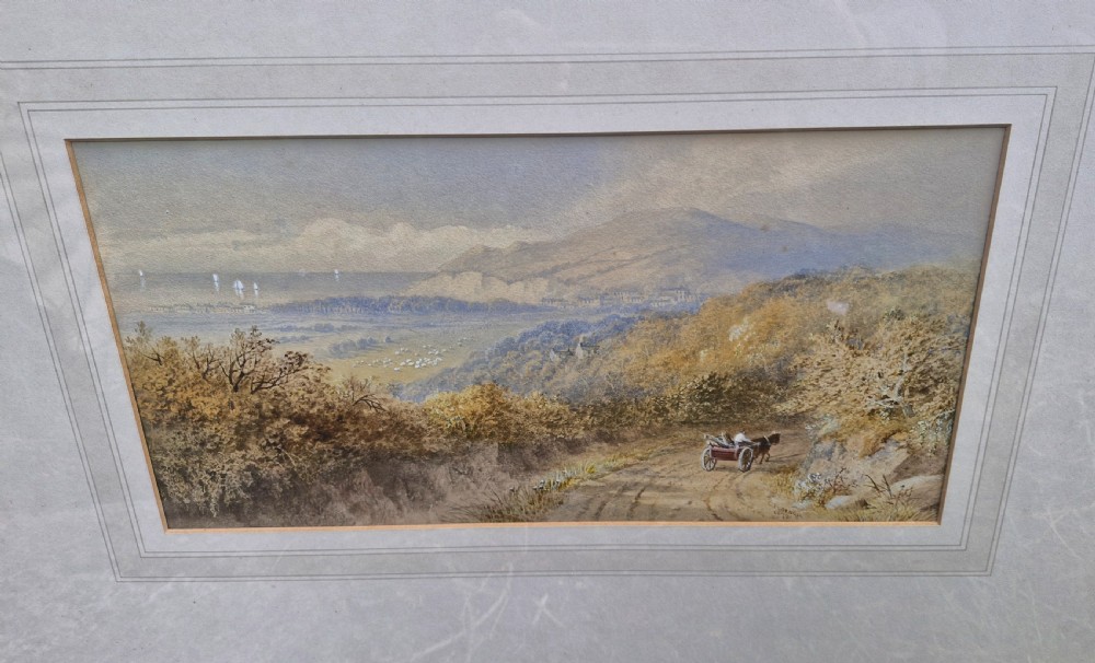 A framed 19th-century watercolour landscape painting showing a horse-drawn cart on a dirt track overlooking hills and the sea, housed within a wide mount and a slim gold frame. View VII