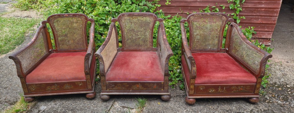 A set of three low-built chinoiserie bergere armchairs featuring hand-painted lacquered frames, woven cane backs and sides, and red velvet seats.