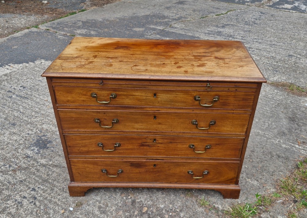 An early nineteenth-century mahogany chest of four graduated drawers featuring brass swan-neck handles, key escutcheons, a pull-out brushing slide, and bracket feet.