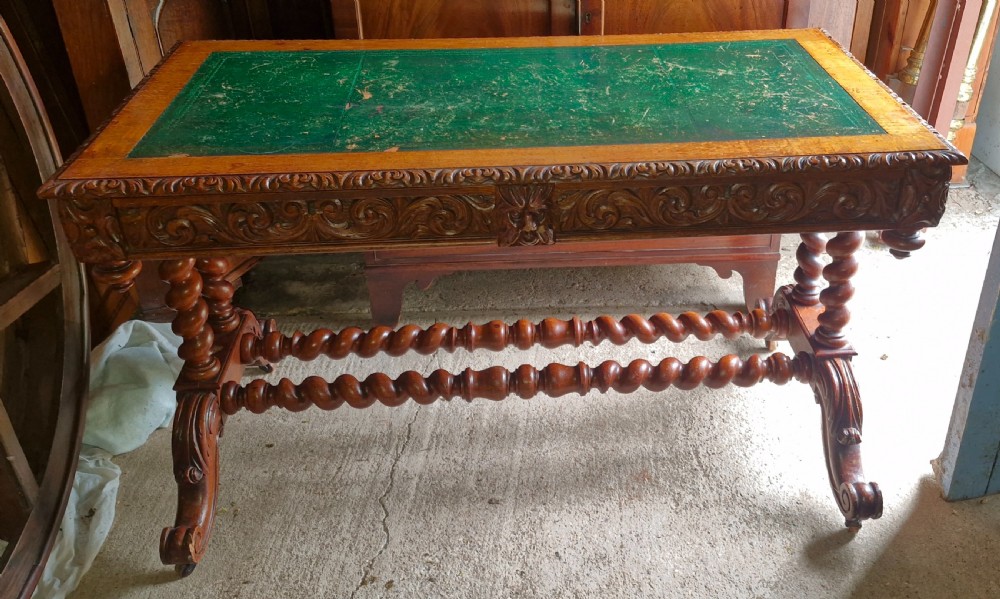 A Victorian carved oak writing desk featuring a green leather inset top, detailed Green Man mask carvings on the drawers, and turned barley twist stretchers.