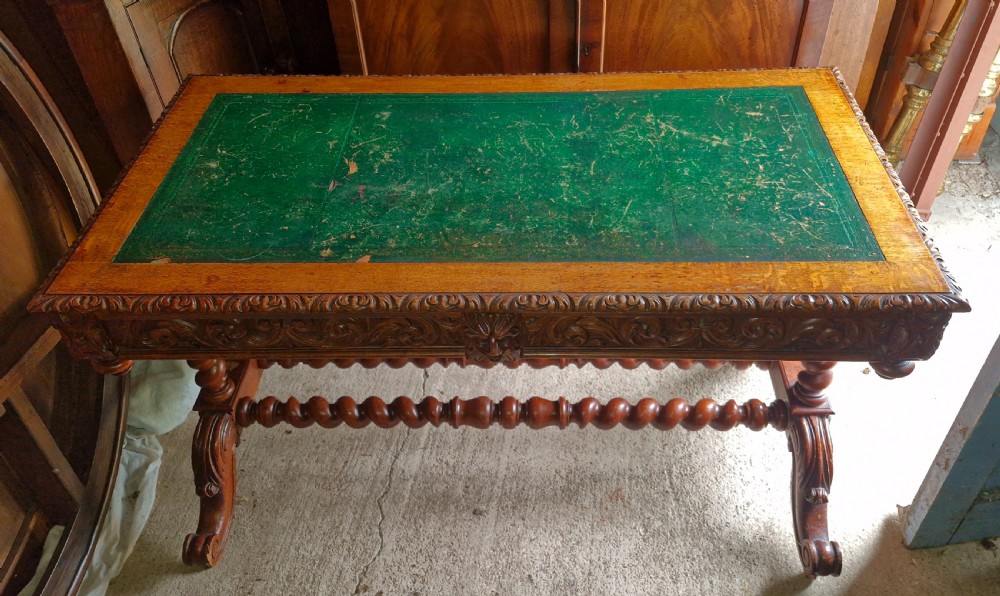 A Victorian carved oak writing desk featuring a green leather inset top, detailed Green Man mask carvings on the drawers, and turned barley twist stretchers. View III