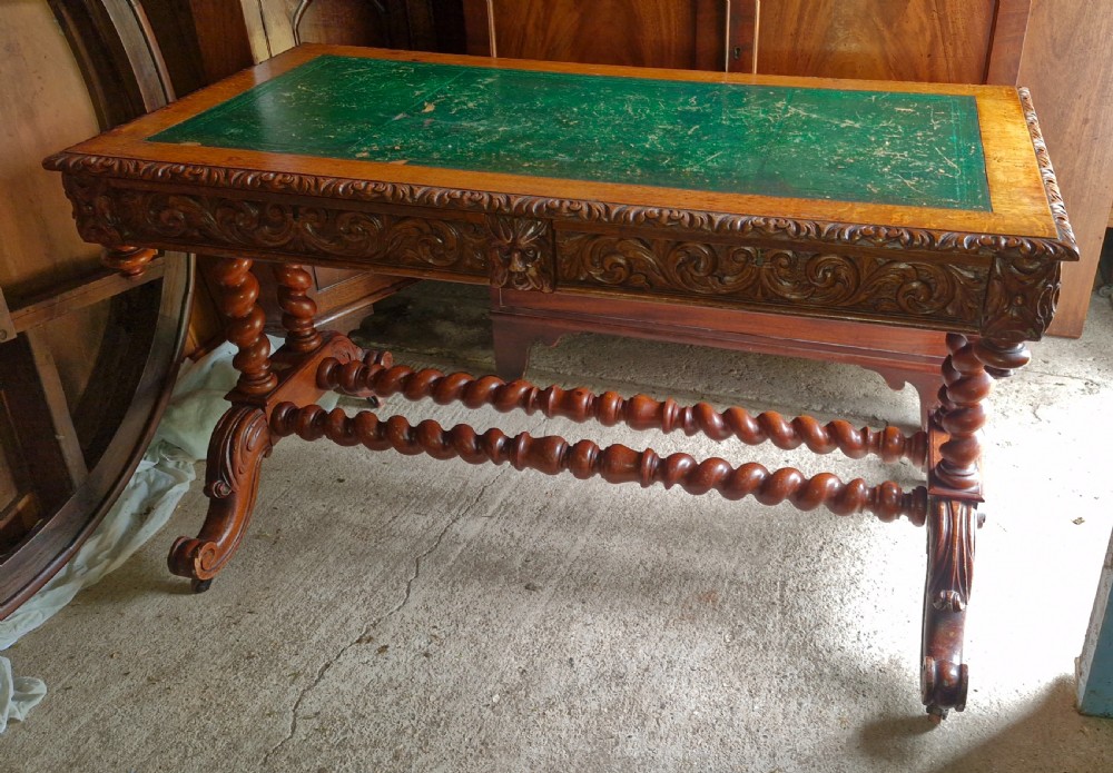 A Victorian carved oak writing desk featuring a green leather inset top, detailed Green Man mask carvings on the drawers, and turned barley twist stretchers. View V