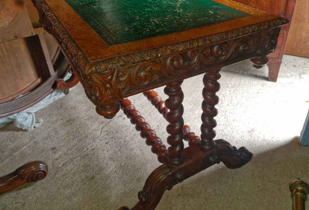 A Victorian carved oak writing desk featuring a green leather inset top, detailed Green Man mask carvings on the drawers, and turned barley twist stretchers. View VII