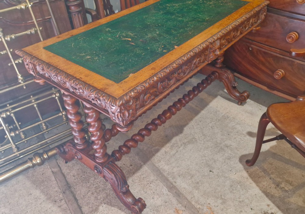 A Victorian carved oak writing desk featuring a green leather inset top, detailed Green Man mask carvings on the drawers, and turned barley twist stretchers. View X