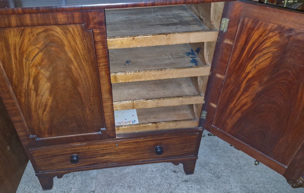 An early 19th-century mahogany dwarf linen cupboard featuring flame mahogany door panels, a single bottom drawer with turned knobs, and shaped bracket feet. View II