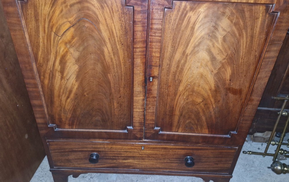 An early 19th-century mahogany dwarf linen cupboard featuring flame mahogany door panels, a single bottom drawer with turned knobs, and shaped bracket feet. View III
