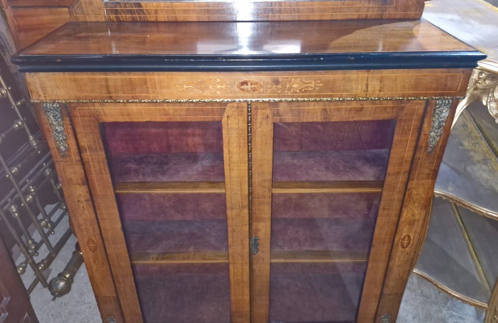 A Victorian walnut side cabinet featuring two glazed doors, decorative marquetry inlay, brass mounts, and an upper gallery shelf with an inset mirror. View III