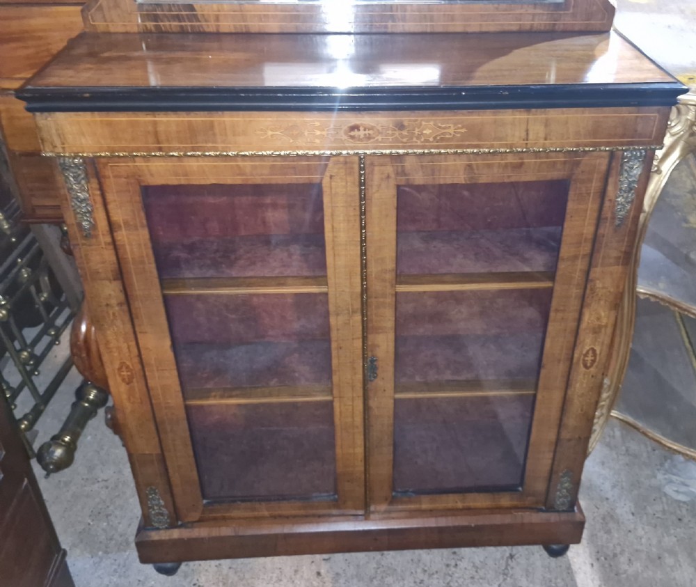A Victorian walnut side cabinet featuring two glazed doors, decorative marquetry inlay, brass mounts, and an upper gallery shelf with an inset mirror. View VII