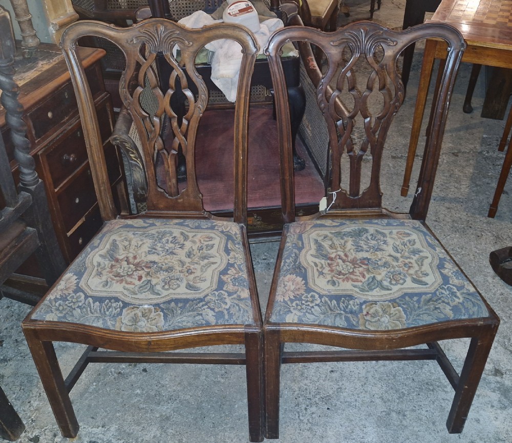 A pair of carved mahogany side chairs featuring openwork pierced splats and floral tapestry upholstered drop-in seats.