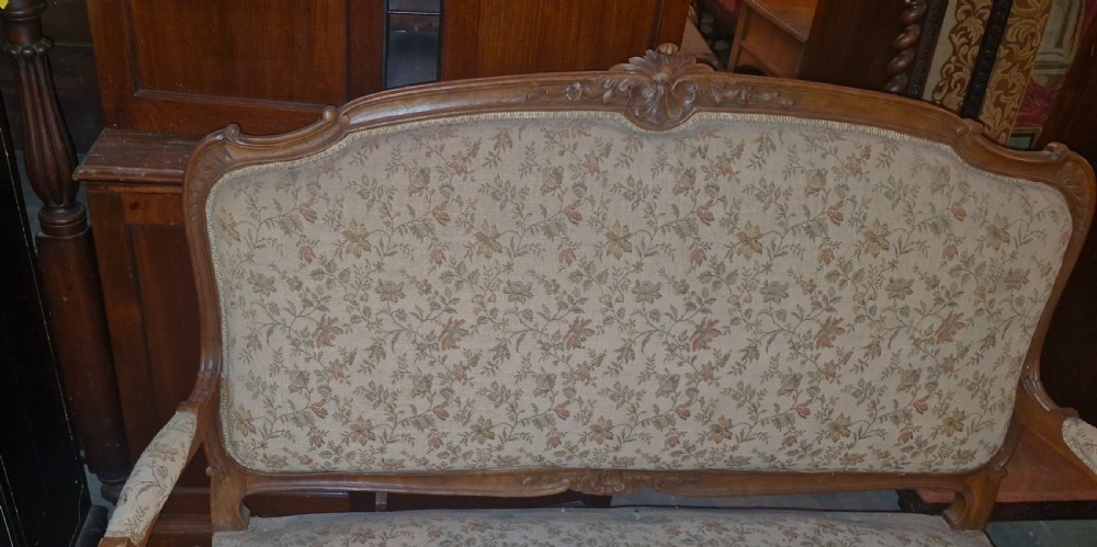 A late 19th-century French walnut canape featuring an exposed carved frame, floral upholstery, padded armrests, and cabriole legs. View VI