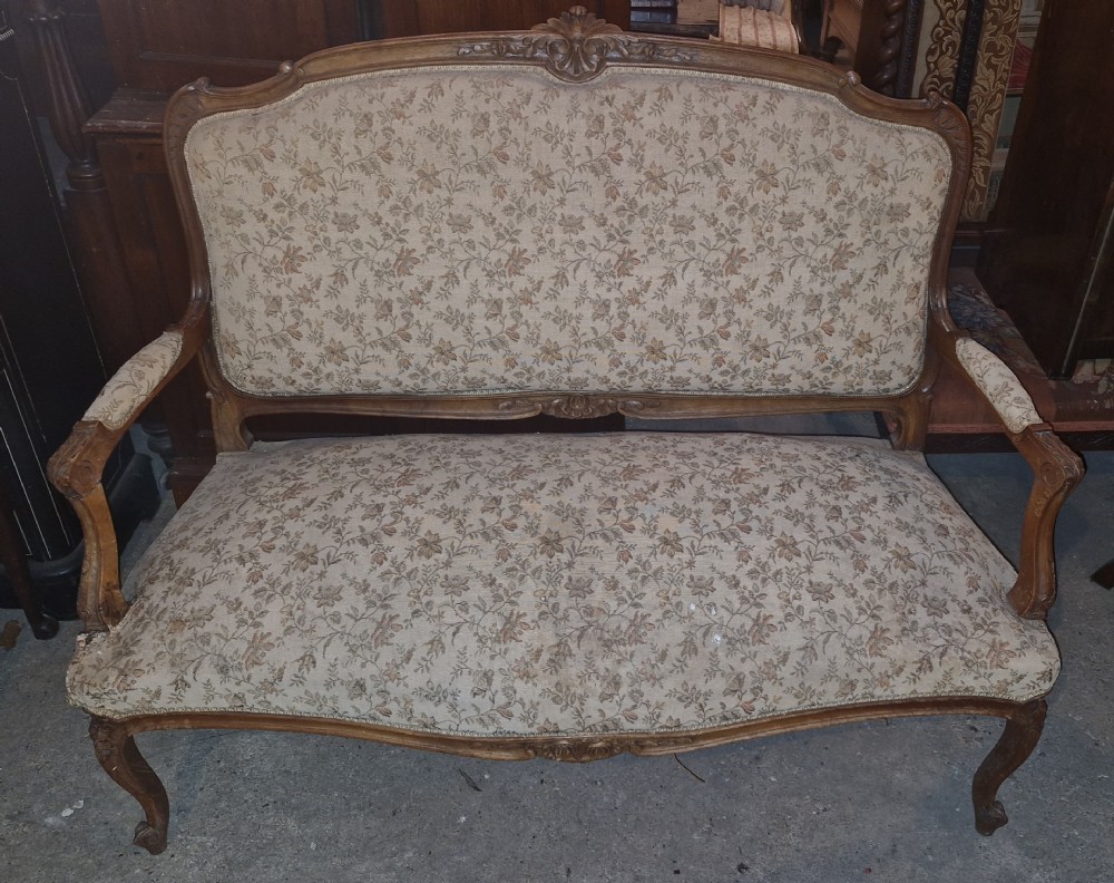 A late 19th-century French walnut canape featuring an exposed carved frame, floral upholstery, padded armrests, and cabriole legs.