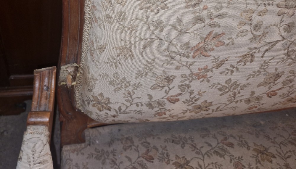 A late 19th-century French walnut canape featuring an exposed carved frame, floral upholstery, padded armrests, and cabriole legs. View X