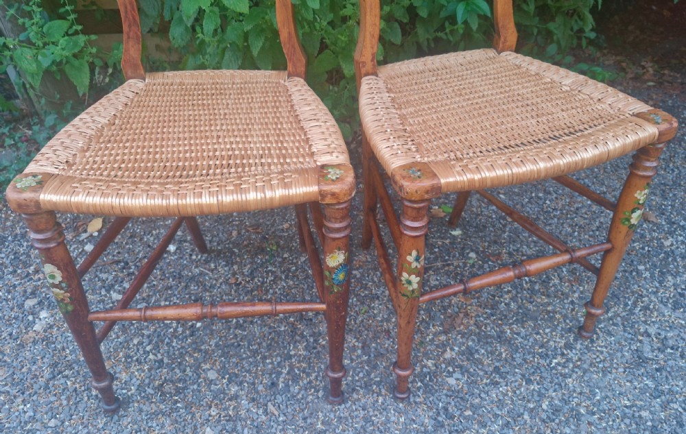 A pair of Victorian side chairs featuring light brown wooden frames adorned with hand-painted floral motifs and woven cane seats. View II