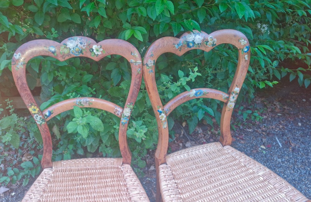 A pair of Victorian side chairs featuring light brown wooden frames adorned with hand-painted floral motifs and woven cane seats. View III