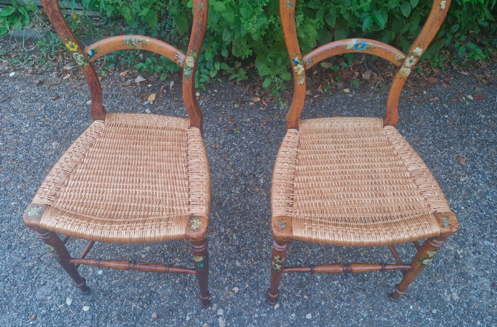 A pair of Victorian side chairs featuring light brown wooden frames adorned with hand-painted floral motifs and woven cane seats. View V